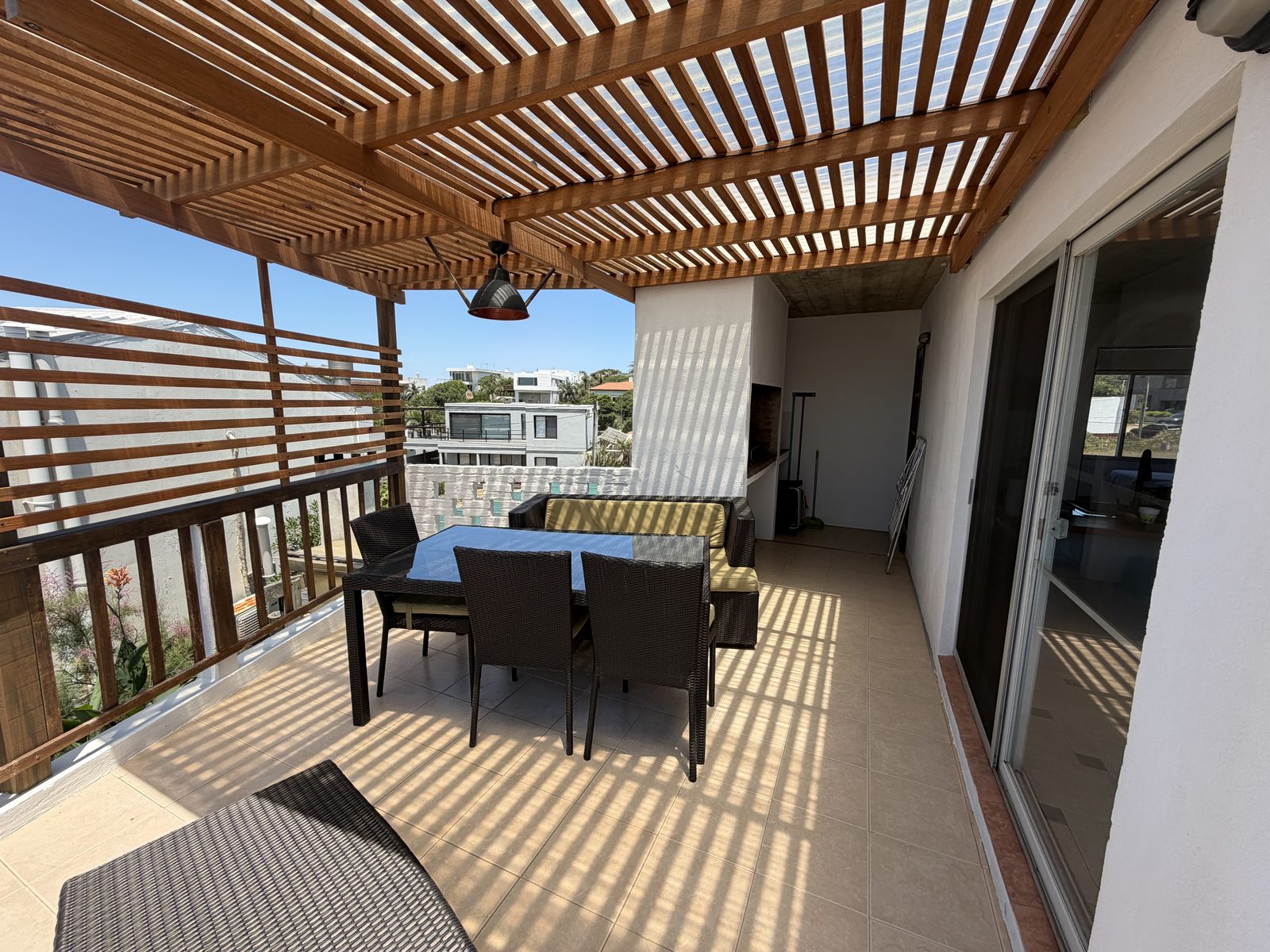 Terraza del bungalow de dos dormitorios, con pérgola de madera, mesa para seis y el parrillero al fondo