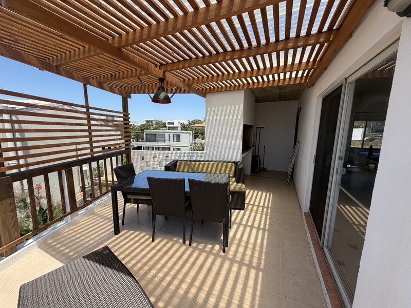 Terraza del bungalow de dos dormitorios, con pérgola de madera, mesa para seis y el parrillero al fondo