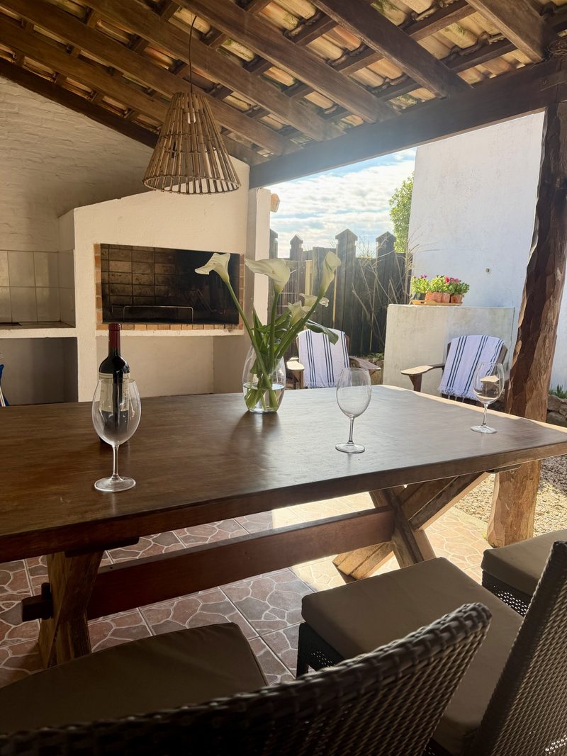 Galería techada del Estudio para 3 personas, con parrillero, mesa de madera y el patio al fondo